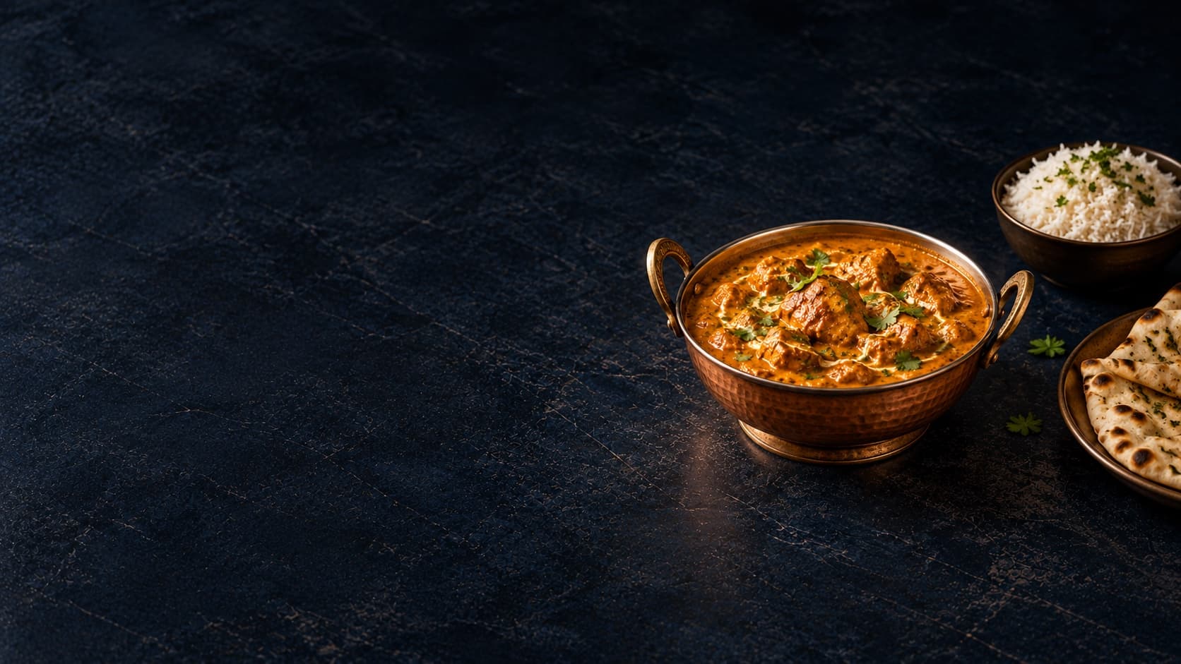 Indian curry in a copper serving bowl with both handles visible on a dark table